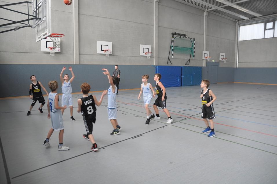 Jugendliche Basketballspieler in blauen und schwarzen Trikots stehen auf dem Spielfeld, während ein Spieler wirft.