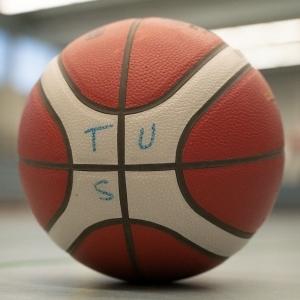 Nahaufnahme eines Basketballs mit der Aufschrift „TUS“ auf einer Sportfläche.