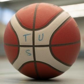 Nahaufnahme eines Basketballs mit der Aufschrift „TUS“ auf einer Sportfläche.