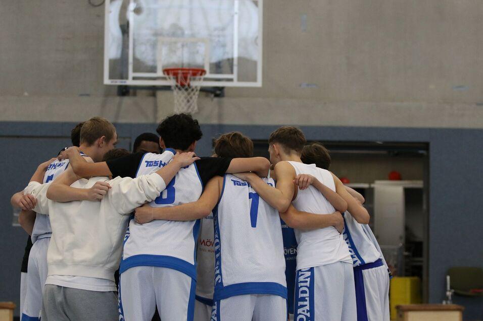 Gruppe von Basketballspielern in Trikots, die sich mit umschlungenen Armen in einer Teamumarmung versammelt haben.