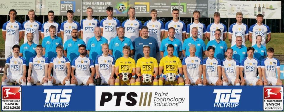 Teambild der Fußballmannschaft Tus Hiltrup mit Trainern und Spielern in blauen und weißen Trikots auf einem Sportplatz.
