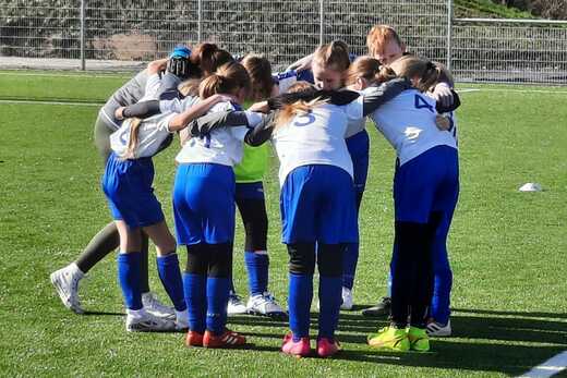 Gruppe von Mädchen in Sportkleidung versammelt sich im Kreis auf einem Fußballplatz, um vor dem Spiel zu besprechen.
