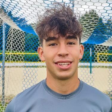 Porträt eines jungen Fußballspielers in grauem Trikot vor einem Fußballtor mit Netz.