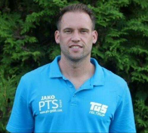 Mann in blauer Sportbekleidung steht vor einem grünen Hintergrund aus Pflanzen.
