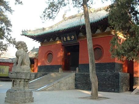 Historisches chinesisches Gebäude mit roten Wänden und geschwungenem Dach, flankiert von Steinskulpturen.