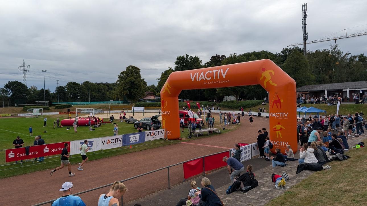 Läufer passieren einen großen orangen Zieleinlauf von "VIACTIV" bei einer Sportveranstaltung mit Zuschauern.
