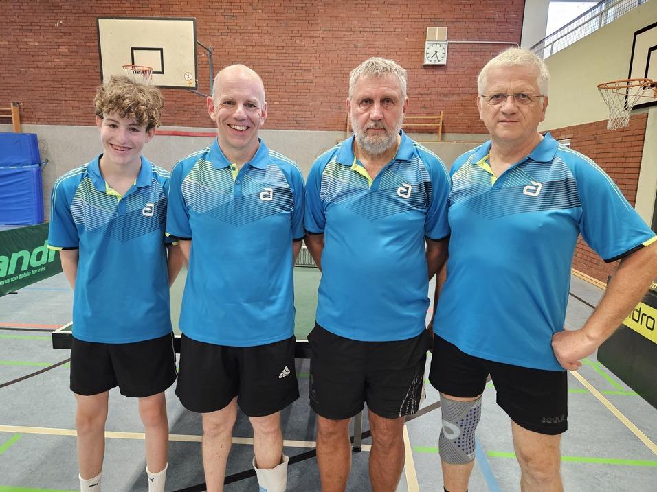 Vier Männer in blauen Tischtennis-Shirts stehen nebeneinander vor einem Tischtennistisch in einer Sporthalle.