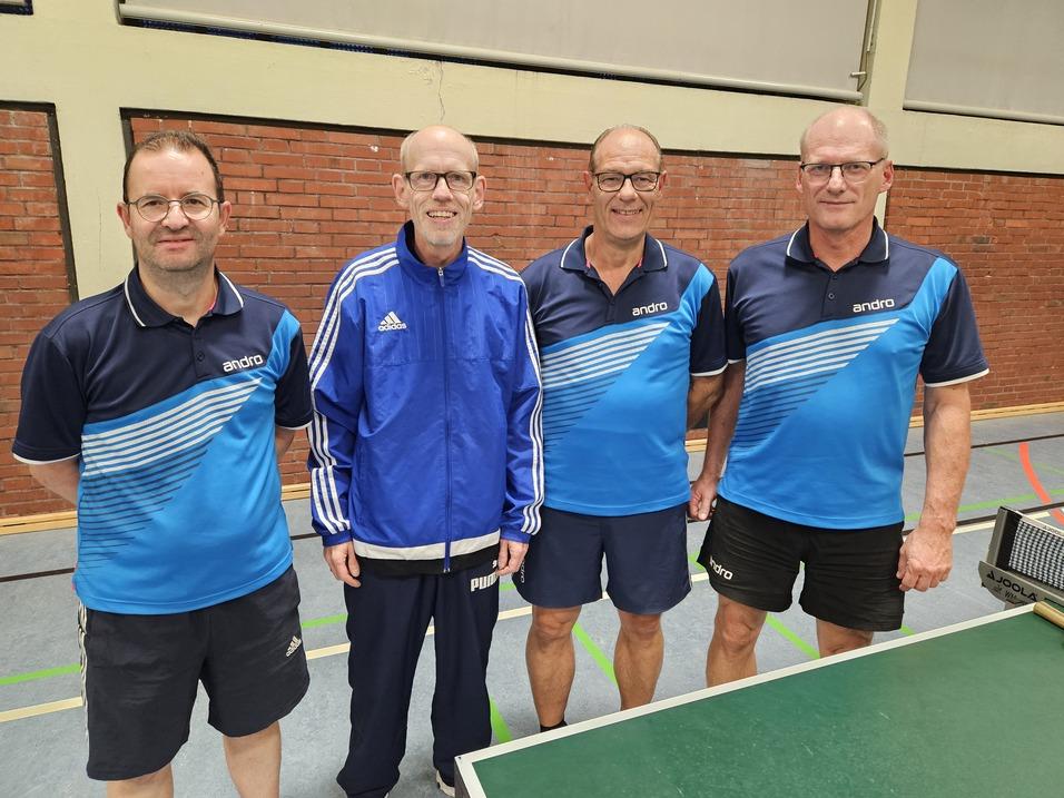 Vier Tischtennisspieler in Sportkleidung stehen lächelnd vor einer Tischtennisplatte in einer Sporthalle.