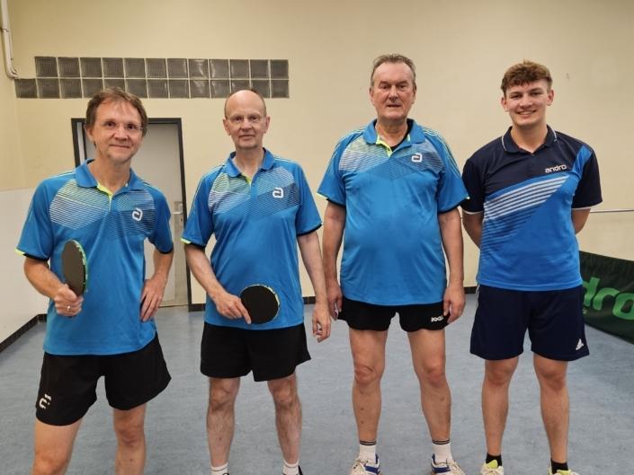 Vier Männer in blauen Tischtennis-Trikots stehen auf einer Tischtennisplatte, jeder mit einem Schläger in der Hand.
