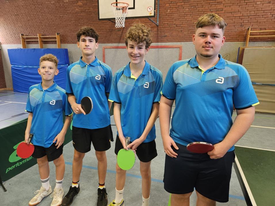 Vier Jugendliche in blauen Tischtennistrikots halten Tischtennisschläger in einer Sporthalle.