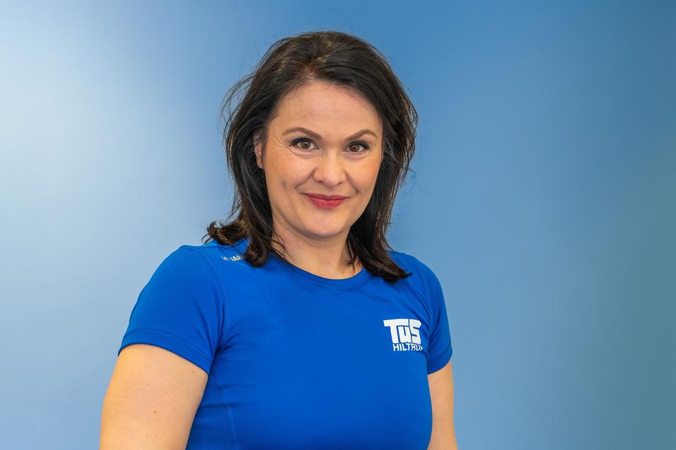 Porträt einer lächelnden Frau in blauem Sportshirt vor einfarbigem Hintergrund.