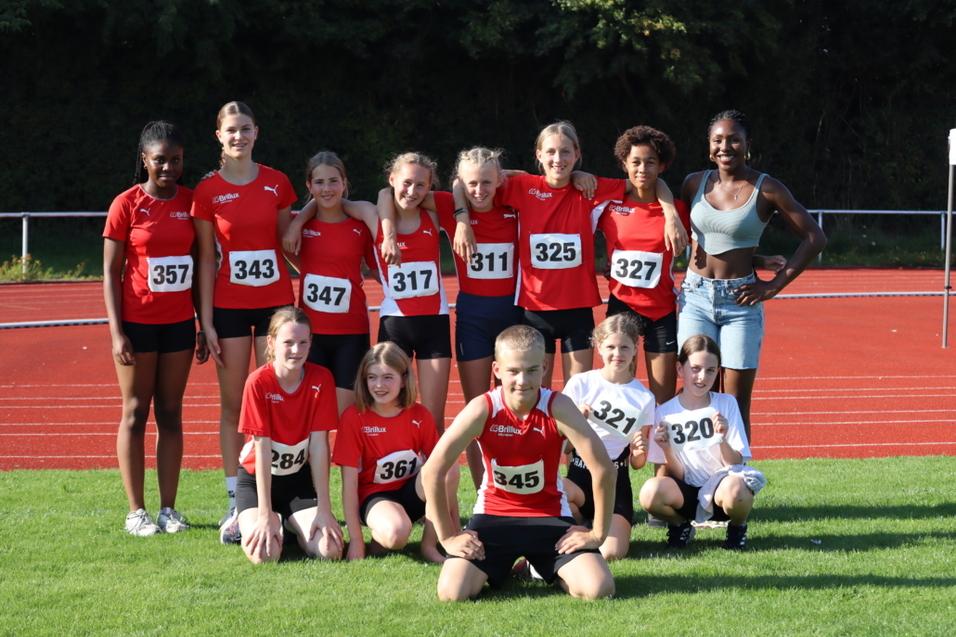 Gruppe von Jugendlichen in Sportkleidung auf einer Leichtathletikanlage, alle lächeln in die Kamera.